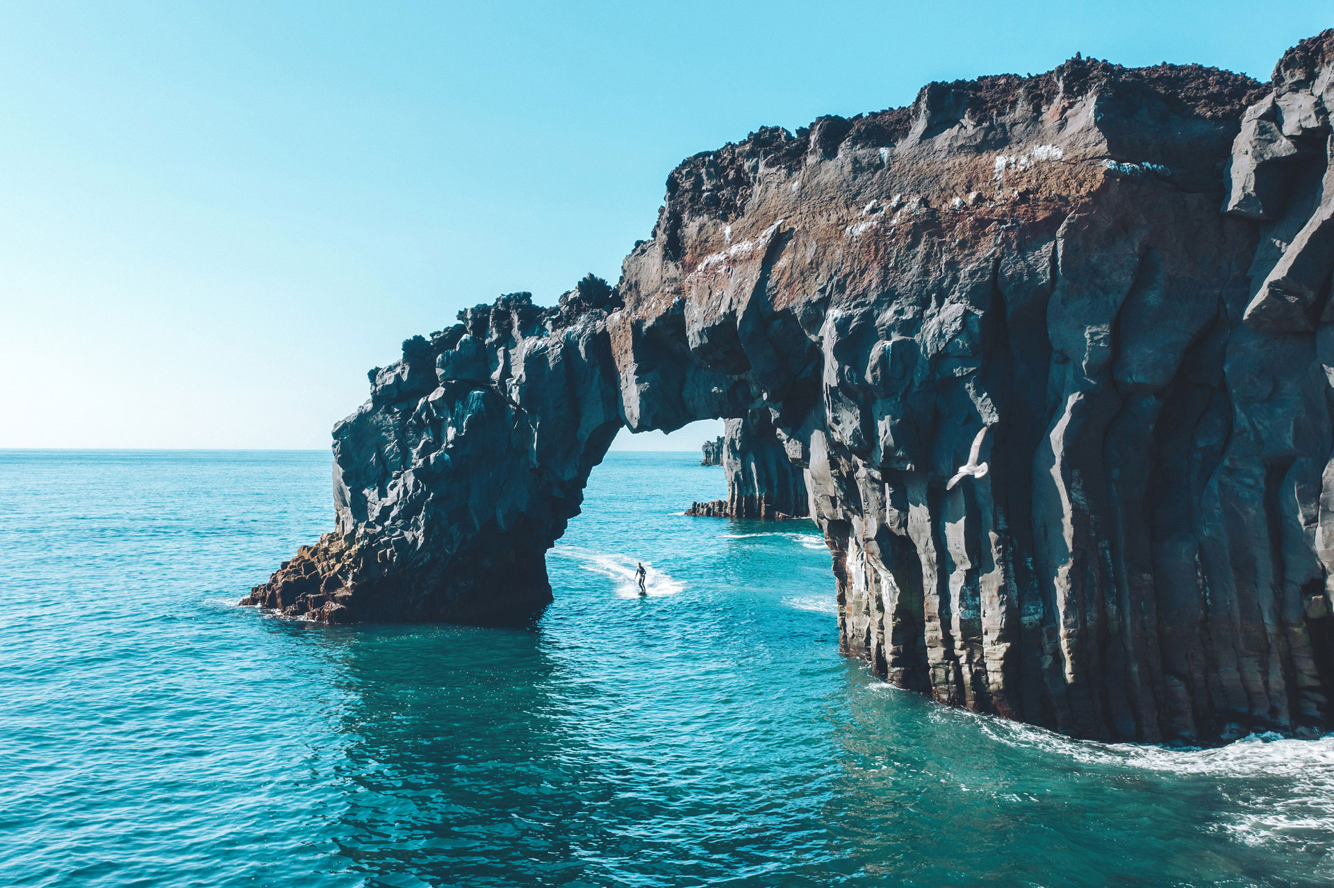 montagne avec falaise, un surfeur passe entre deux roches